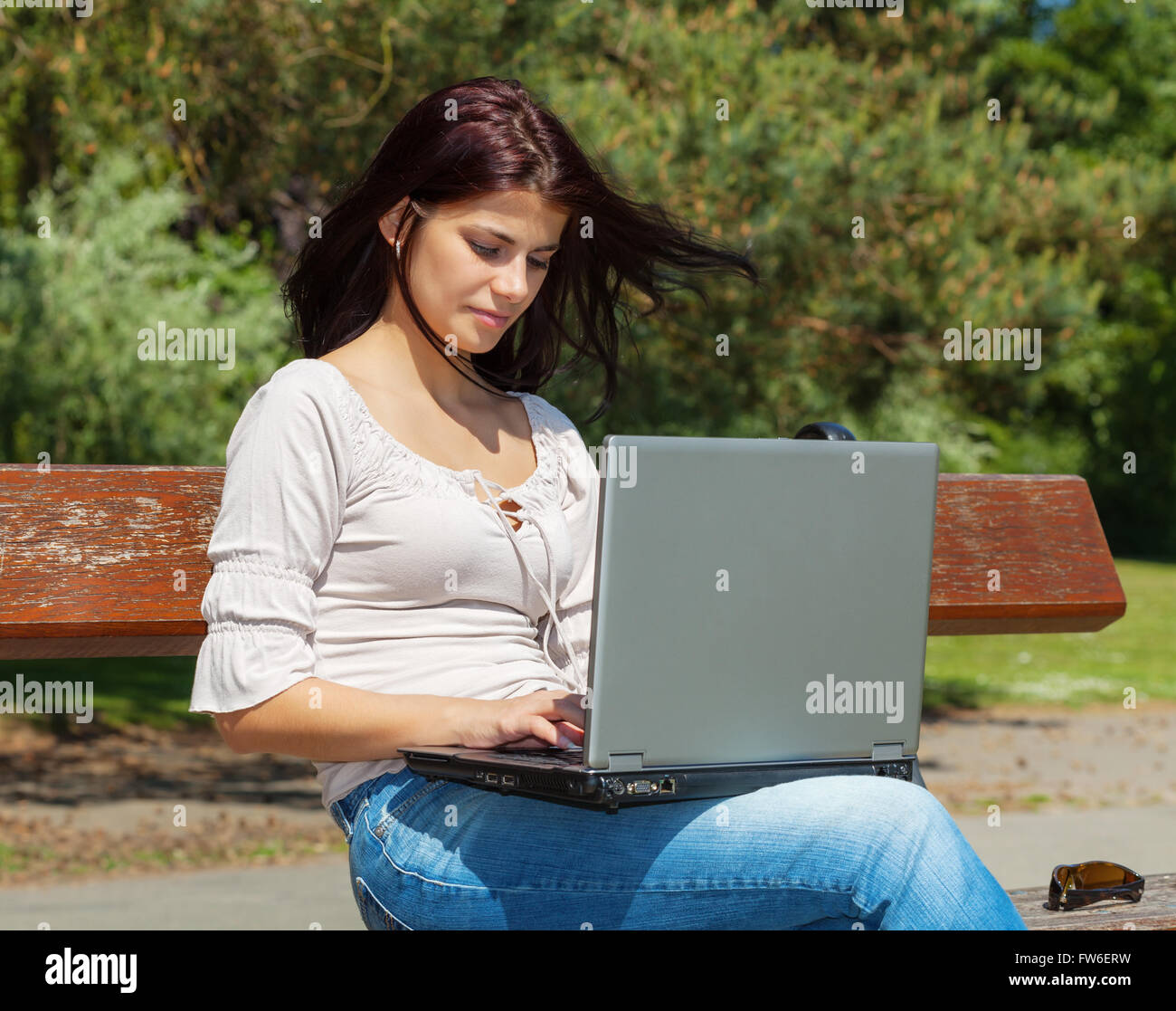Young woman sitting on a bench with laptop computer in a bright sunny day Stock Photo
