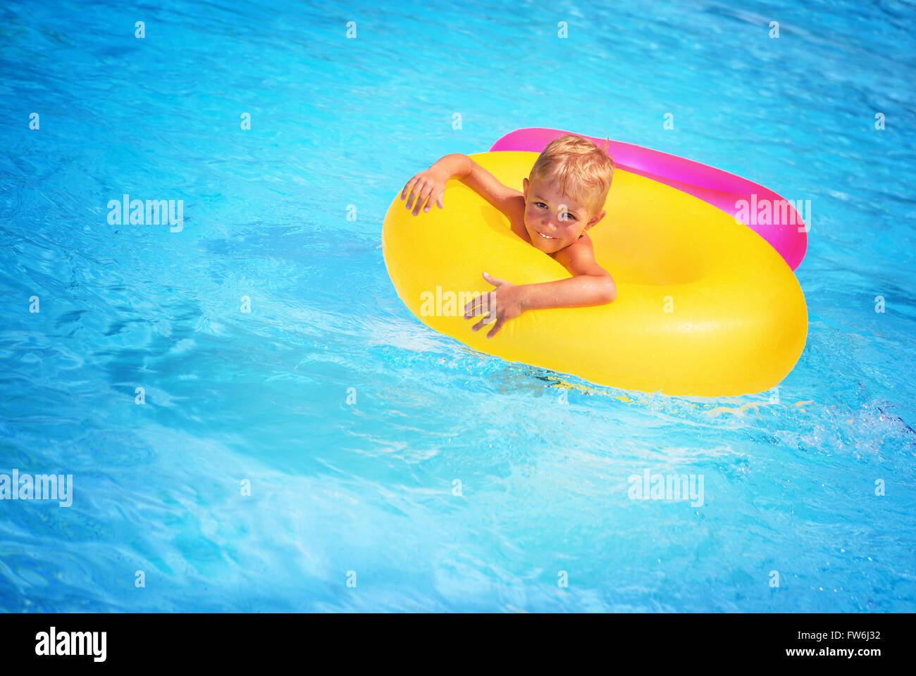 Cute happy little boy having fun in swimming pool, floating in blue refreshing water with big green rubber ring, active summer Stock Photo