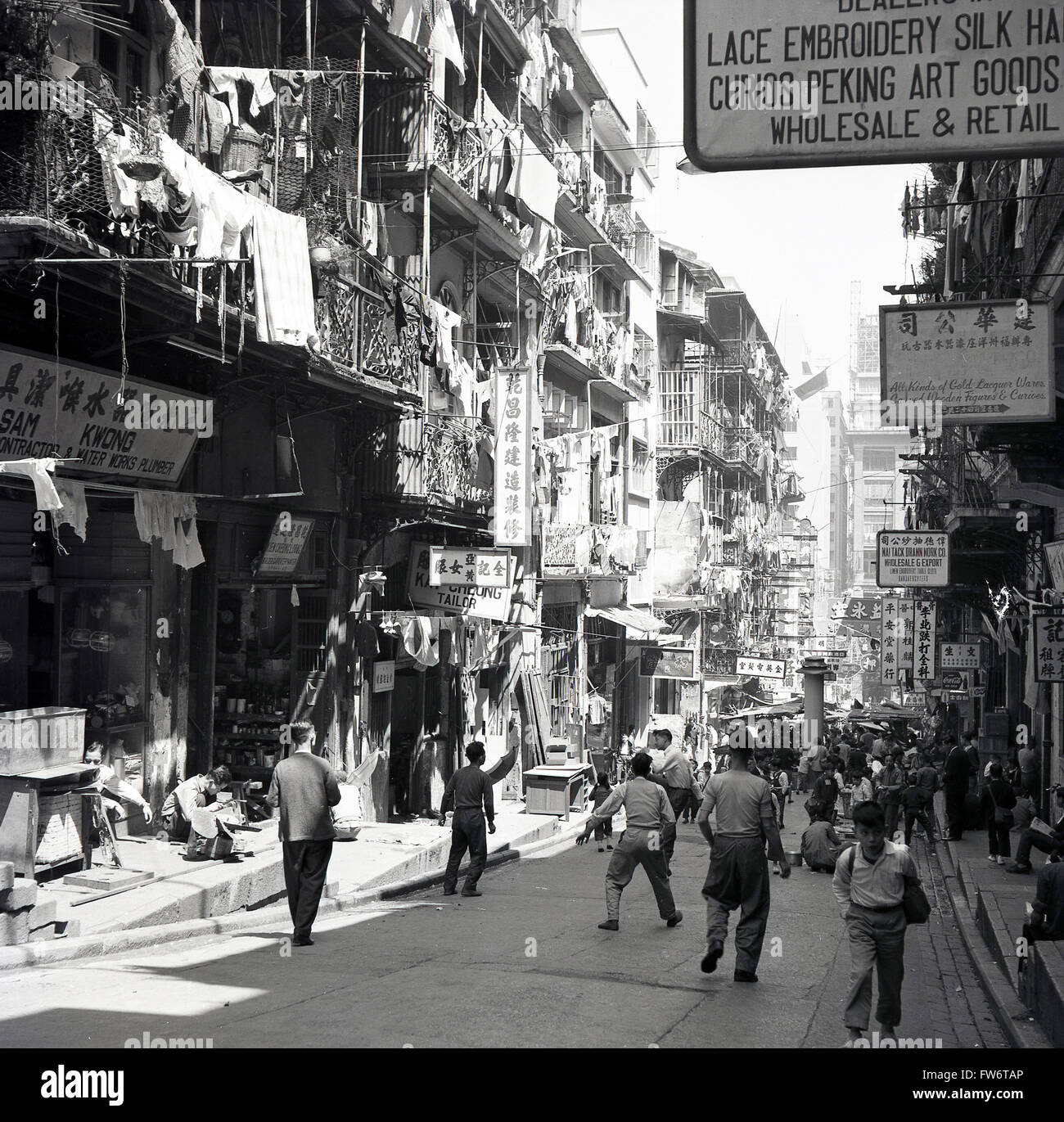 1950s, historical, daytime and a view down a street in the old town of Hong  Kong, showing the layers of different floors above the stores and sellers  at ground level Stock Photo -