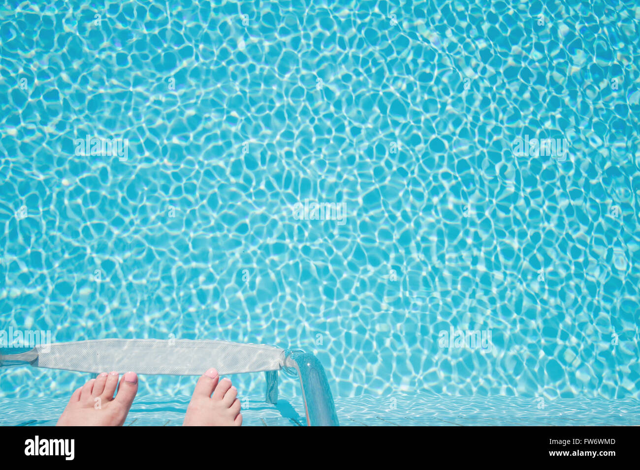 Feet about to climb down ladder into a crystal clear sparkling pool Stock Photo