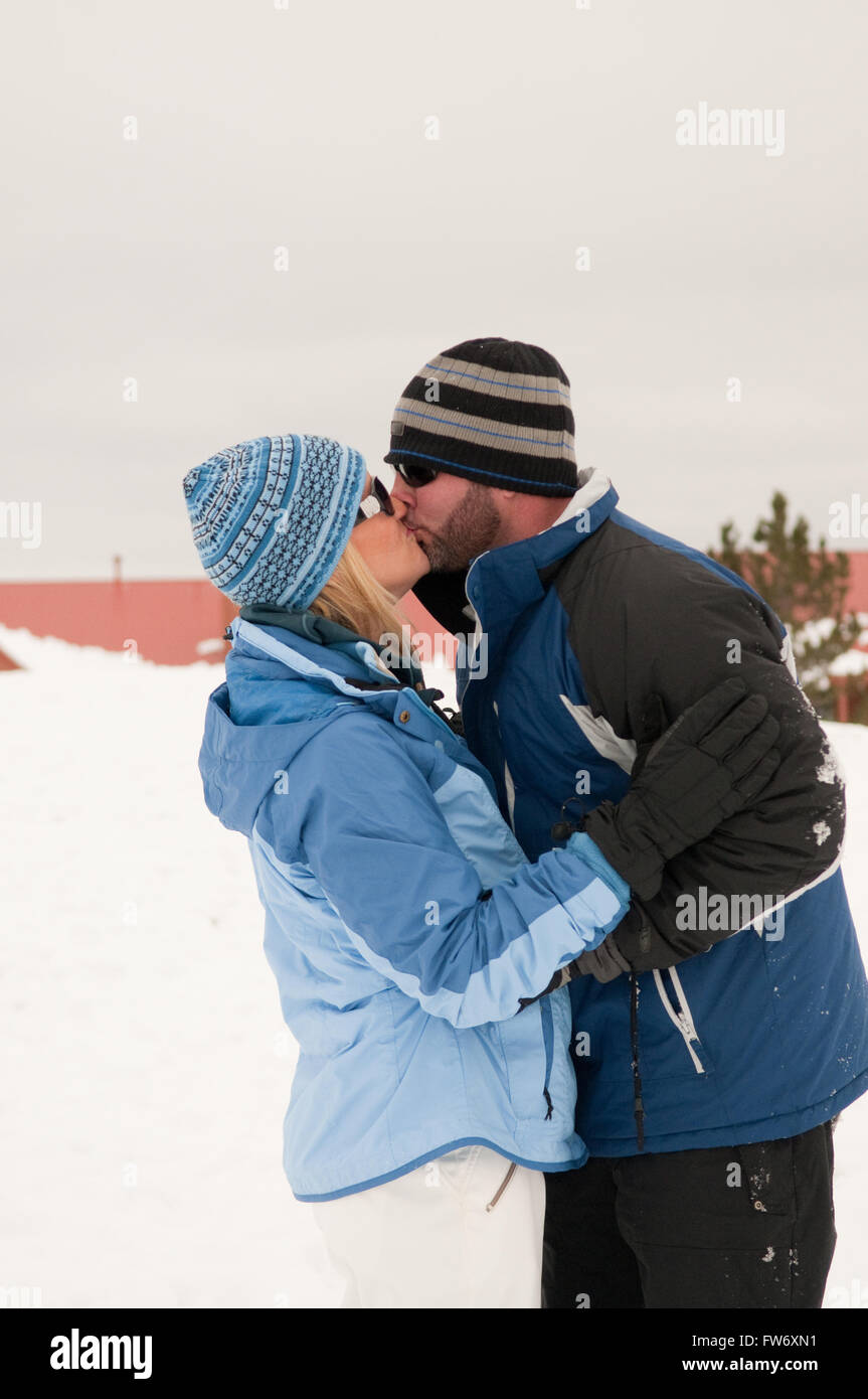 A couple in love on vacation kissing in the snow wearing toboggans and