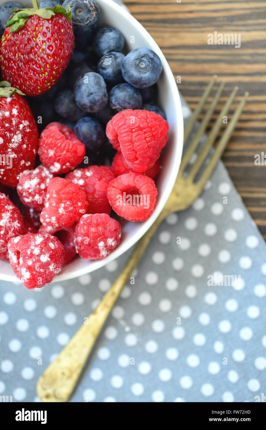 Breakfast bowl of mixed berries on wooden table with fork and polka dot cloth. Stock Photo