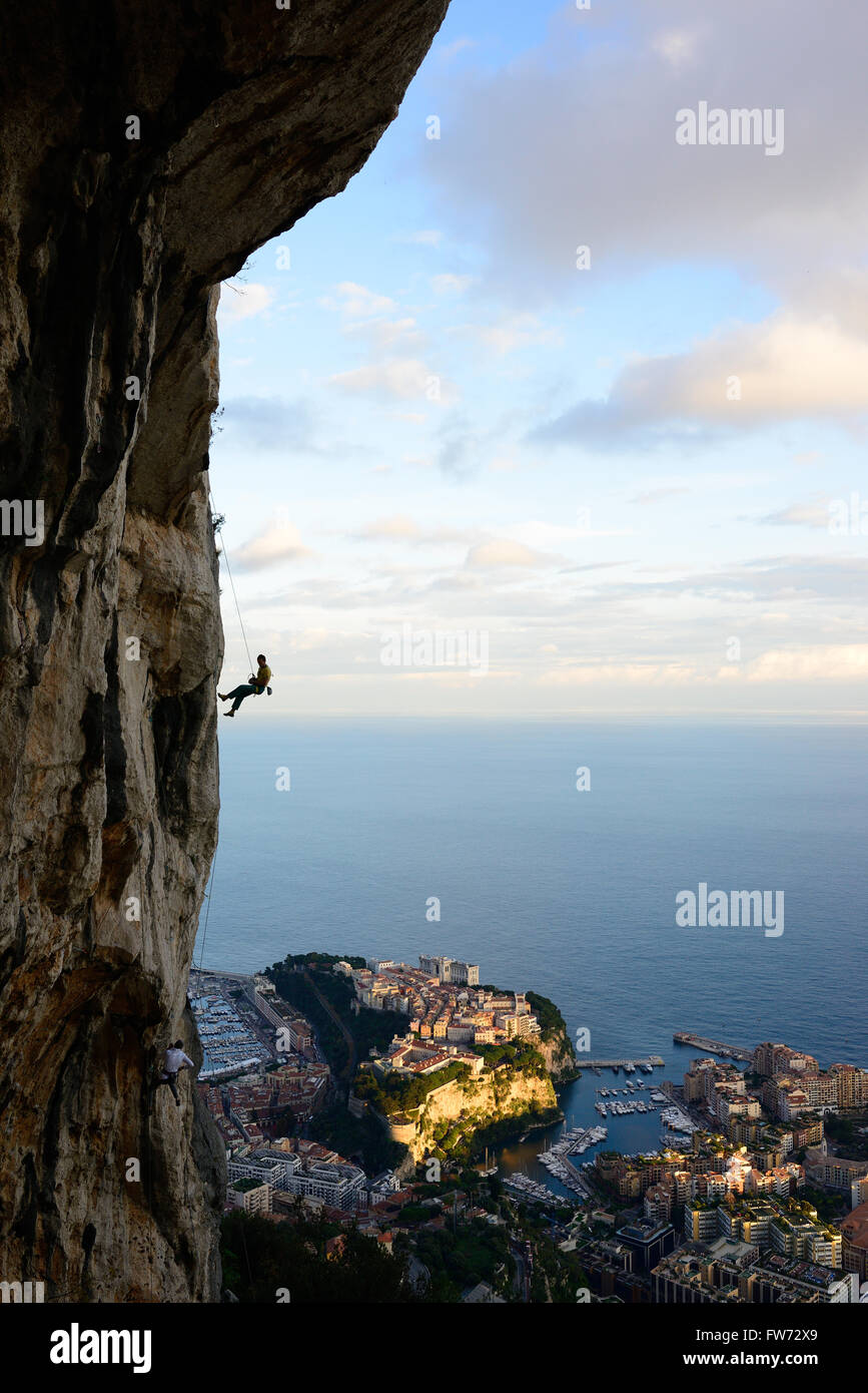 Man abseiling a limestone cliff with Monaco and the Mediterranean Sea for background. La Turbie, Alpes-Maritimes, French Riviera, France. Stock Photo