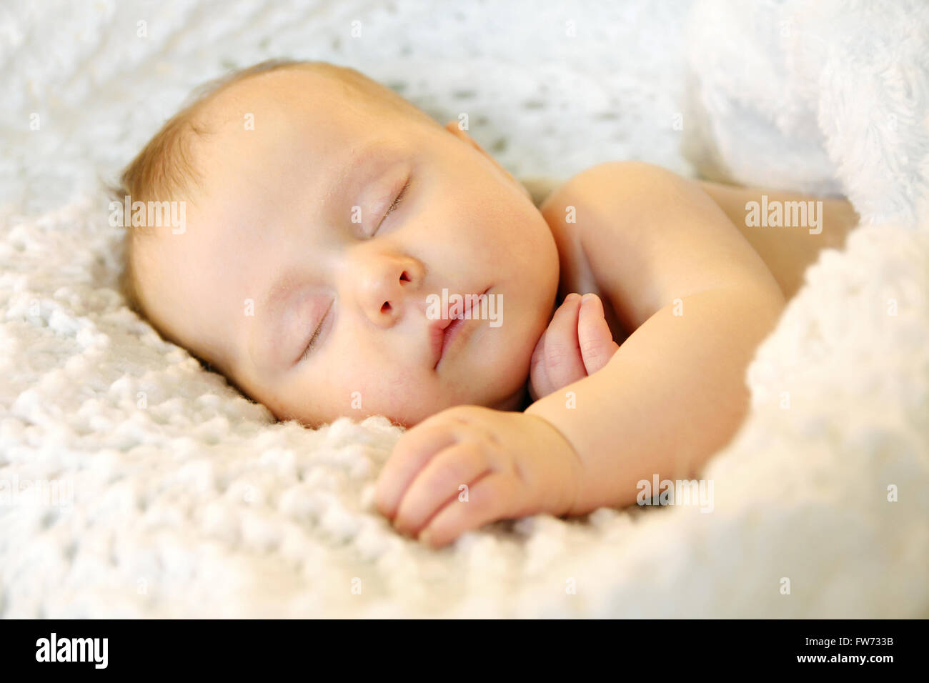 A sweet newborn infant girl is sleeping peacefully while snuggled in warm white blankets Stock Photo
