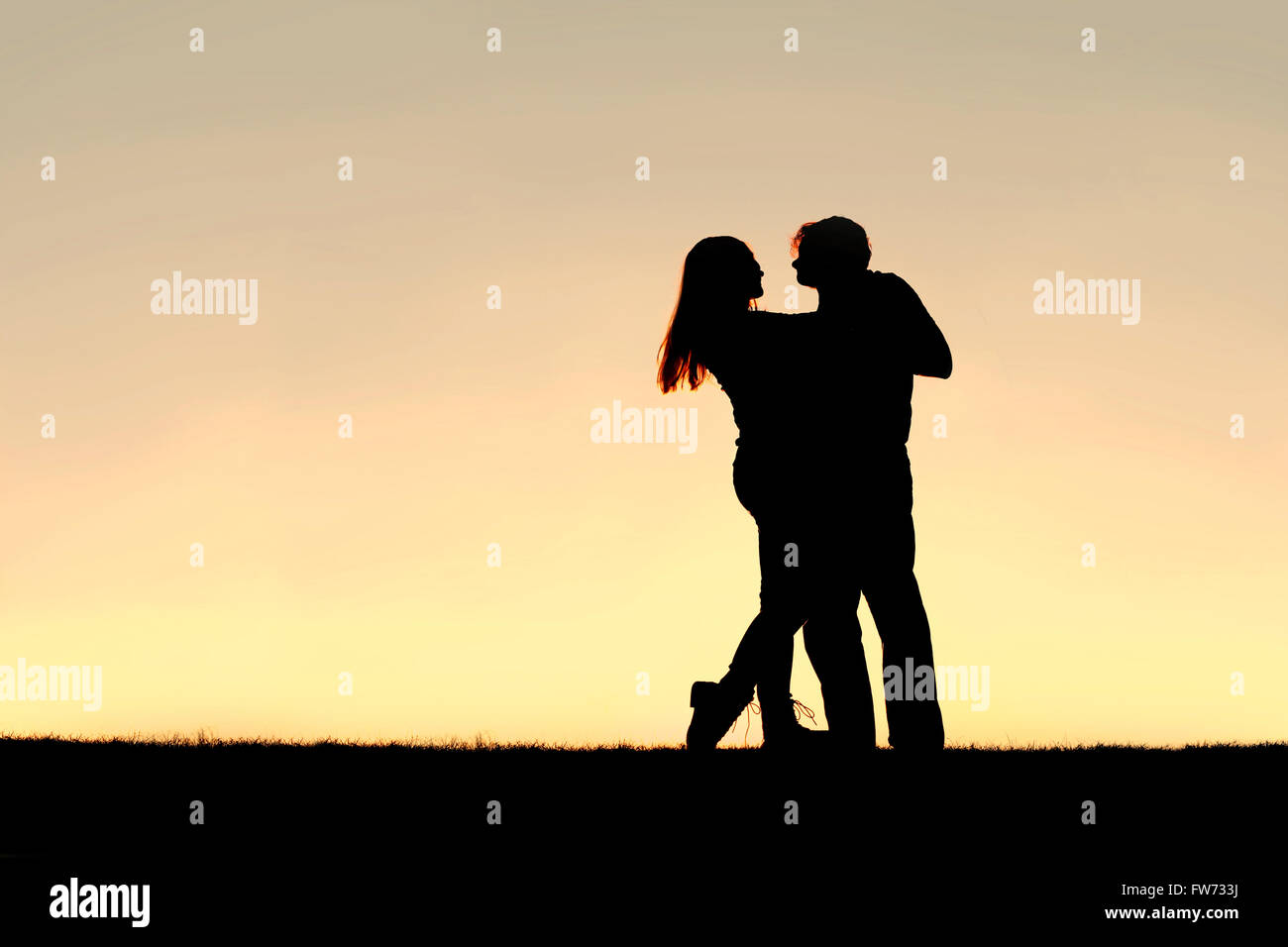 A silhouette of a happy young married couple slow dancing outside at sunset, with copy-space in sky. Stock Photo