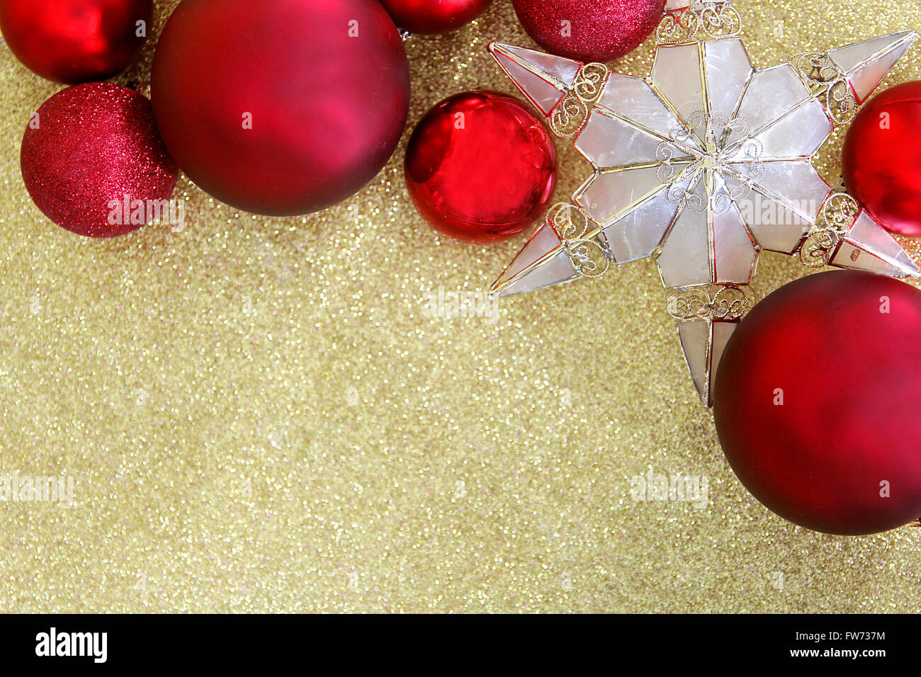 Red Christmas bulb decorations and a star shaped tree topper border the top of a background gold glitter fabric with copy-space. Stock Photo