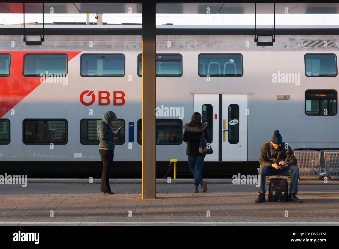 A view of a train and waiting passengers at sunset at Sankt Pölten train station in Austria Stock Photo
