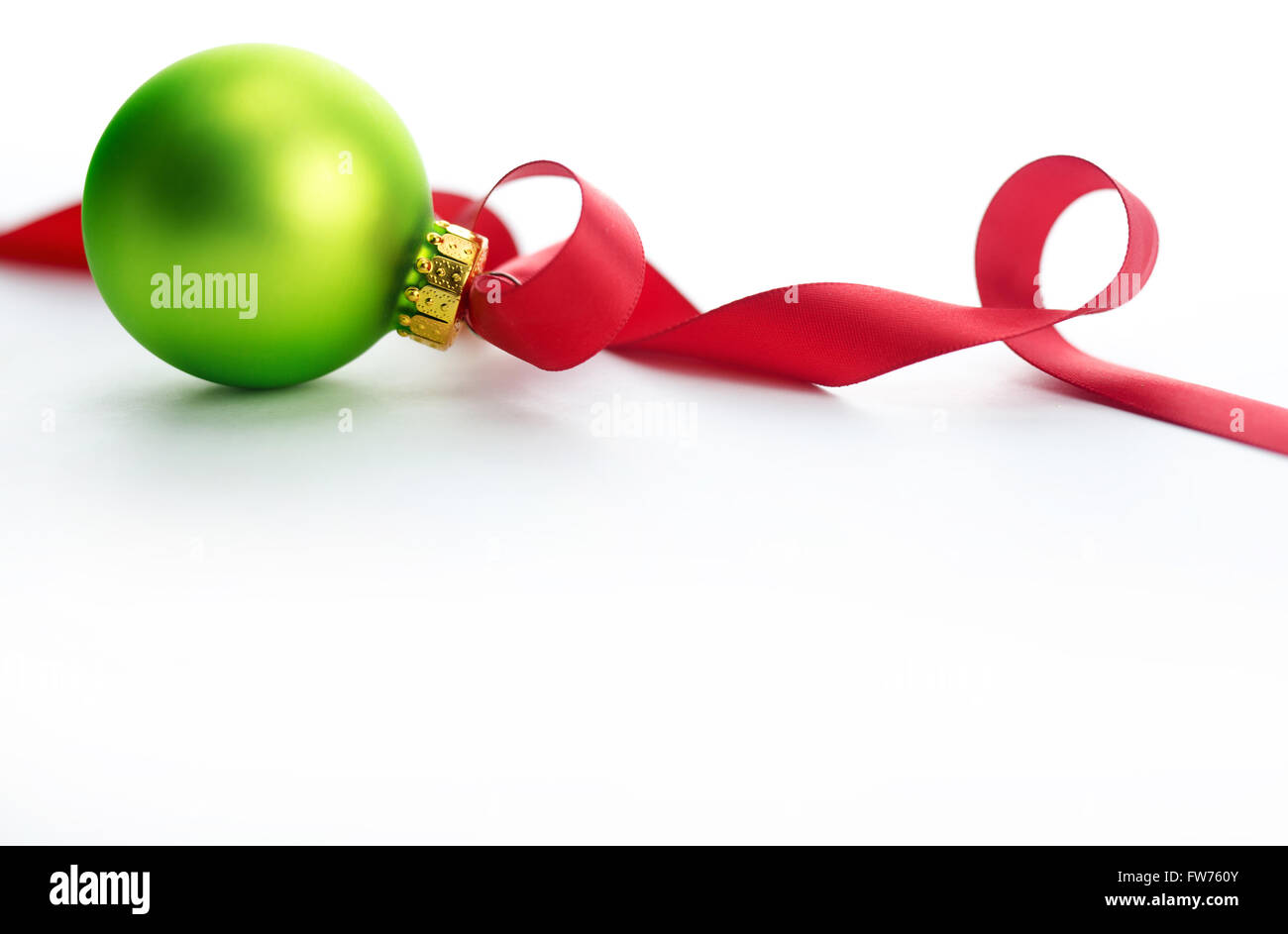 Green glass Christmas ornament with red ribbon on white background