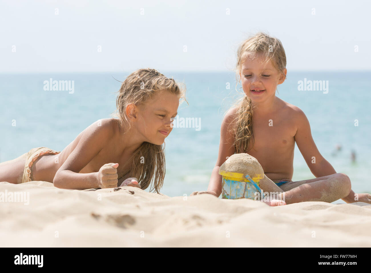 Two little girls are playing with enthusiasm in the sand on the