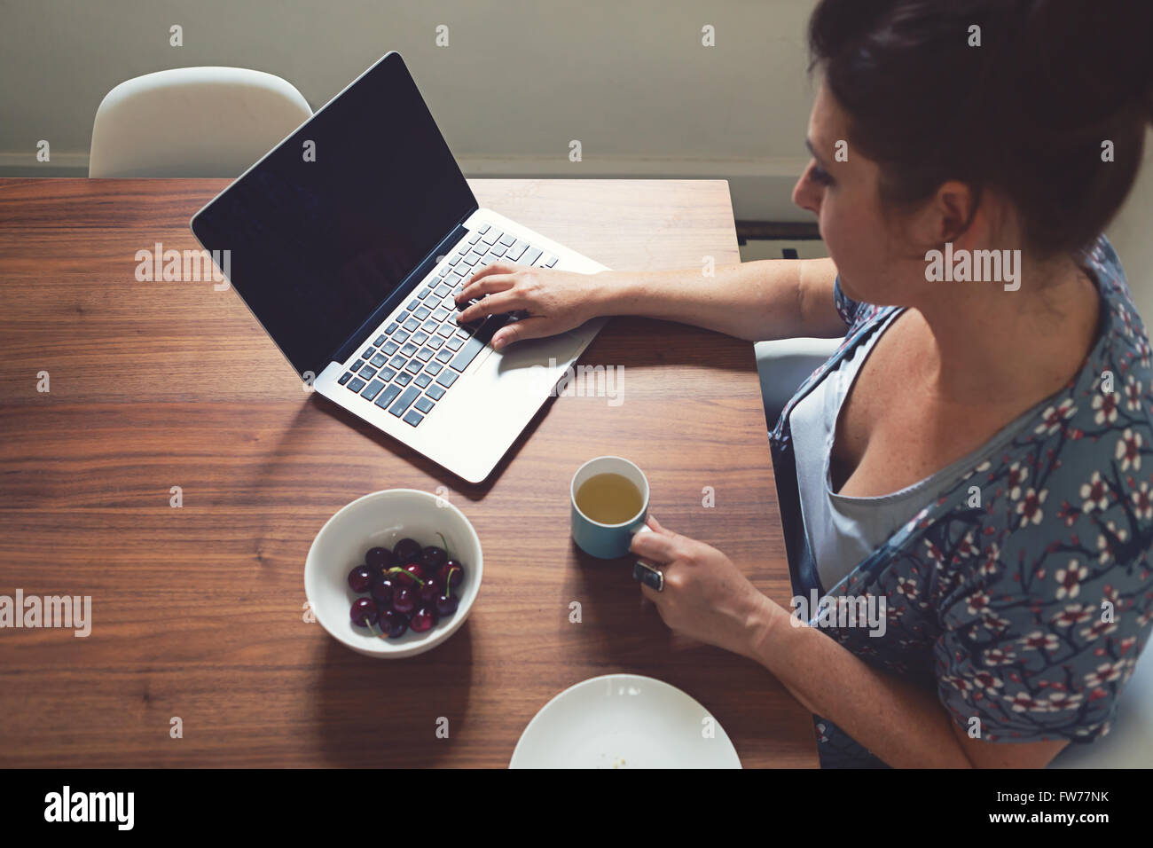 Horizontal overhead of woman working on computer at home with focus on the keyboard and blurred face Stock Photo