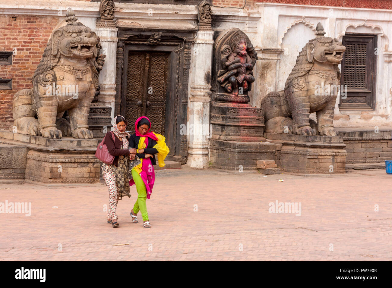 Bhaktapur, Nepal.   Women Walking Past Lions Guarding Entrance to Palace, Durbar Square. Stock Photo