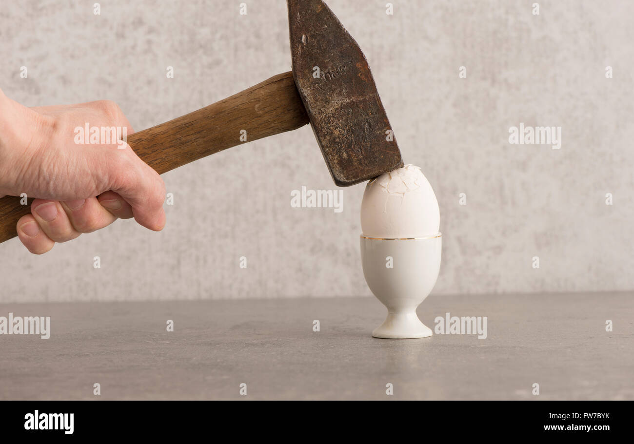 Breakfast egg cracked with hammer. Concept of brutal force, strength and overdoing. Stock Photo