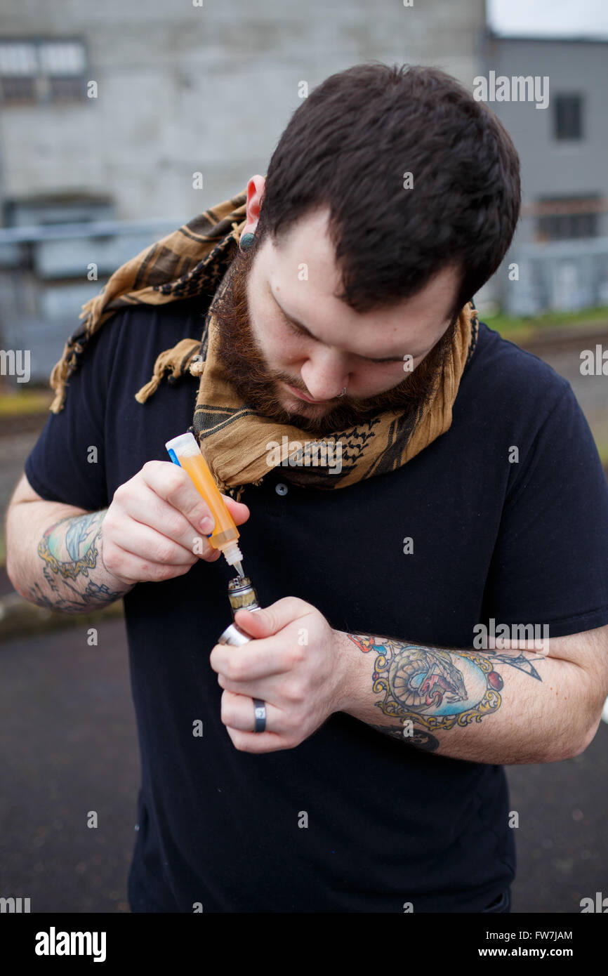 EUGENE, OR - MARCH 20, 2016: Urban portrait of a bearded hipster man with tattoos vaping using a custom mod vape device. Stock Photo