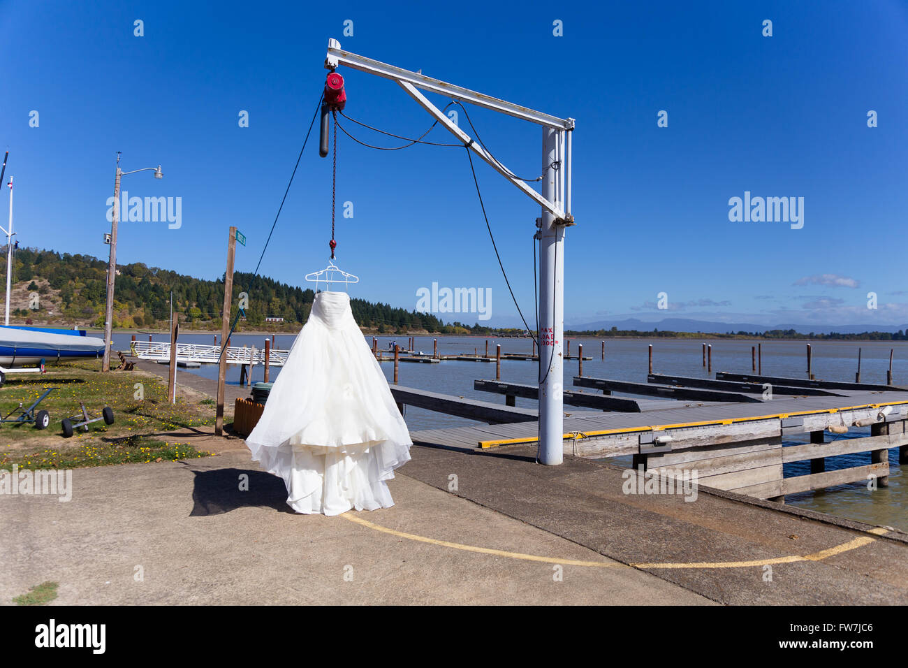 Wedding dress hung from a boat hoist at a yach club marina before the bride puts it on. Stock Photo