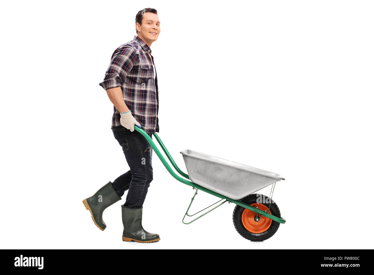Young gardener pushing a wheelbarrow and looking at the camera isolated on white background Stock Photo