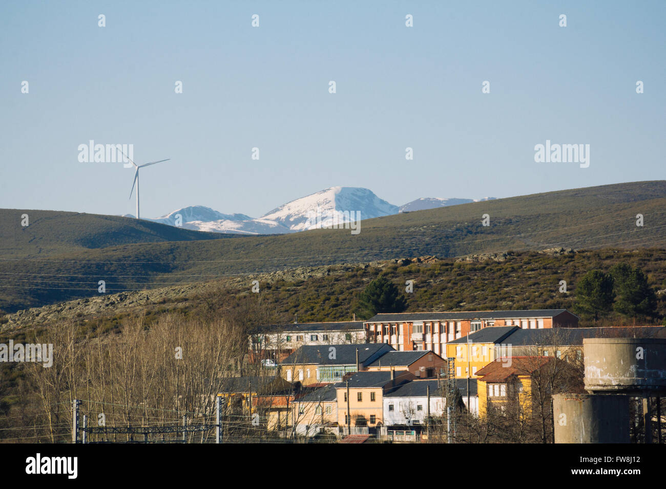 View of a snowed mountain in the distance, a wind farm and a village in the foreground on a sunny day. Stock Photo