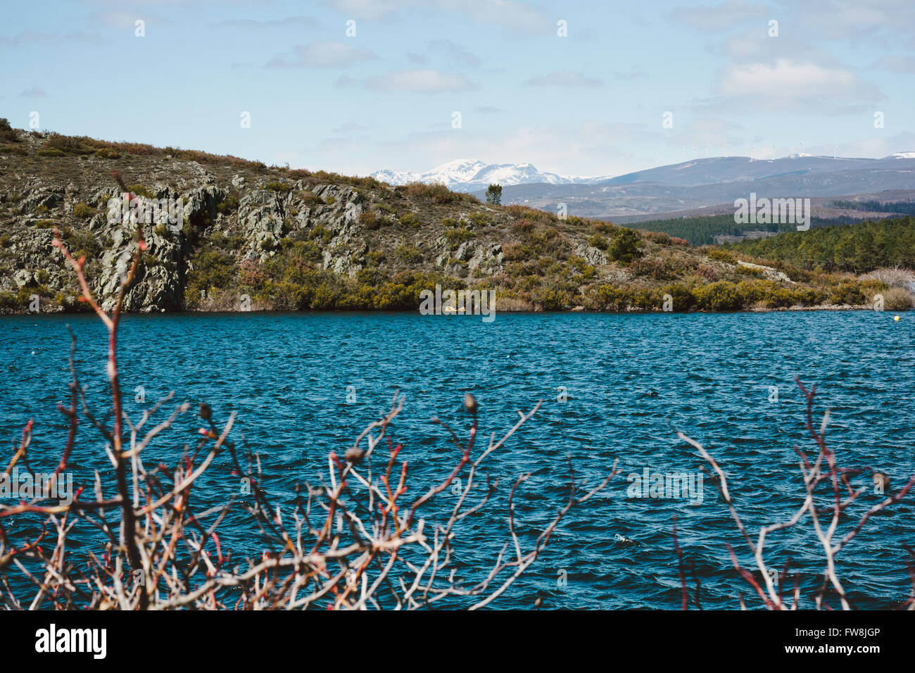 Blue water and mountains in the background with a wind farm and snow on the peaks. Reservoir in Spain. Stock Photo
