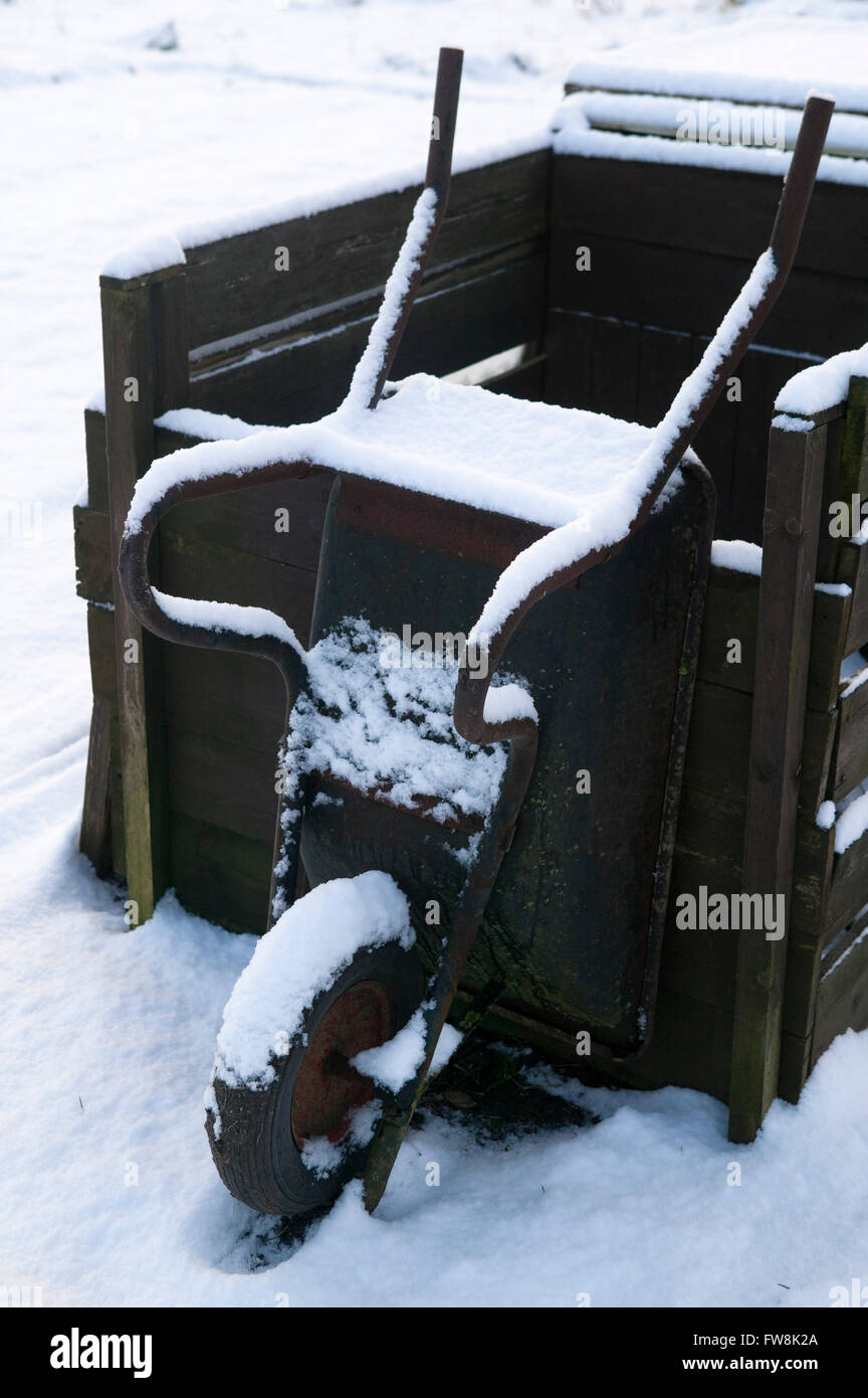 A wheel barow on an allotment leans up and waits for the return of spring as it sts in the snow covered ground in the depths of a frozena dn icey UK winter. Stock Photo