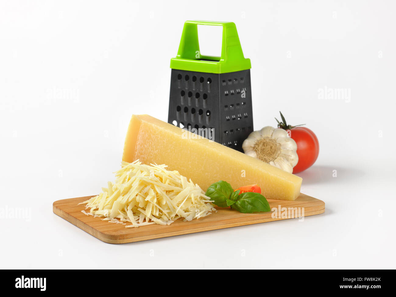 Parmesan Cheese and Grater Medium. an wider view of a block wedge of  parmesan cheese with shredded pieces all around and a metal cheese grater  on a cutting board Stock Photo