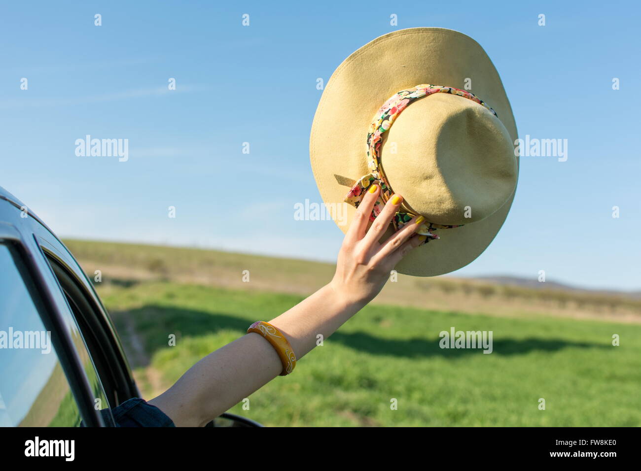 Woman hand with a hat thru car window. Travel time Stock Photo