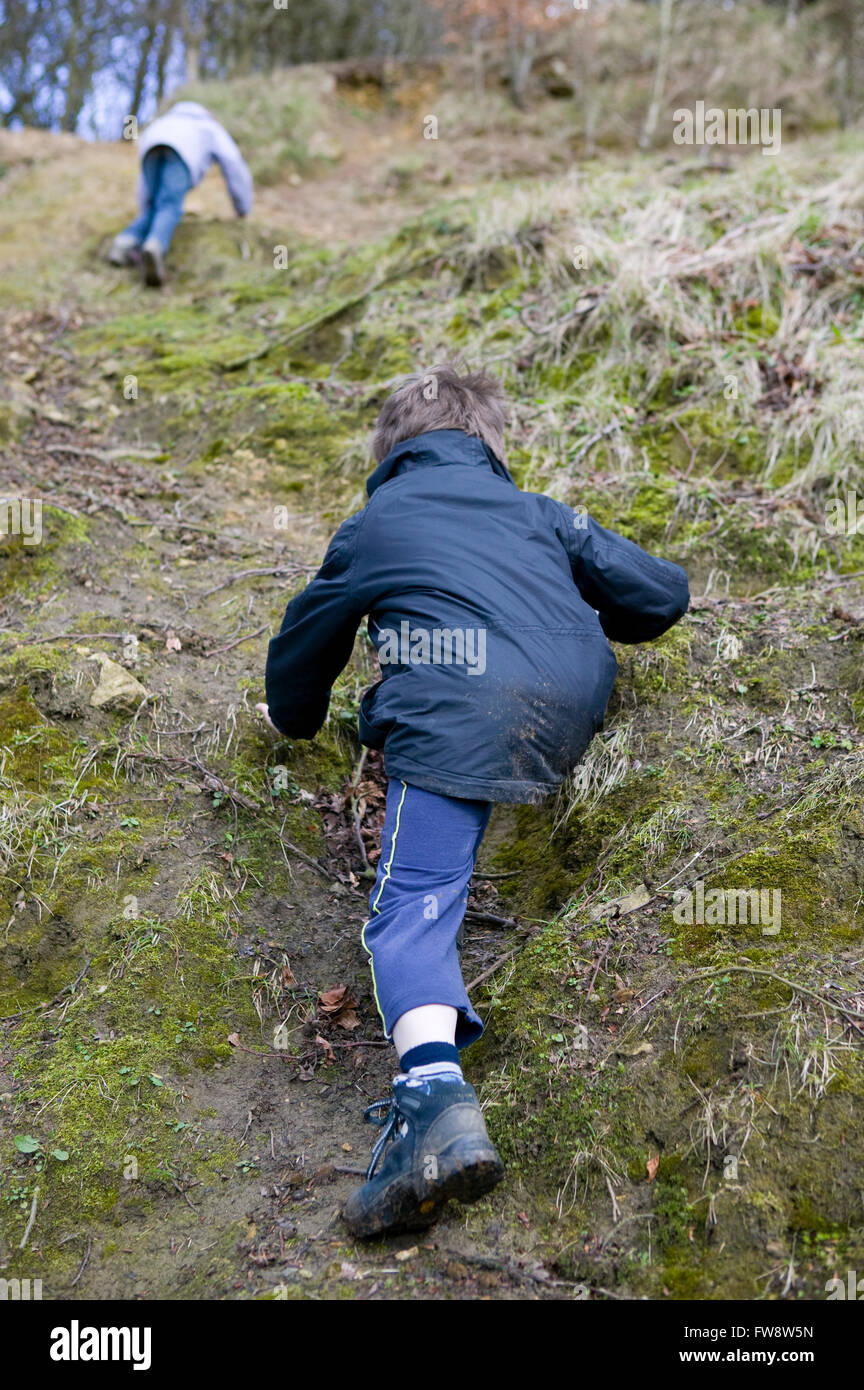 Two children on a country adventure climbing a very steep hill, using
