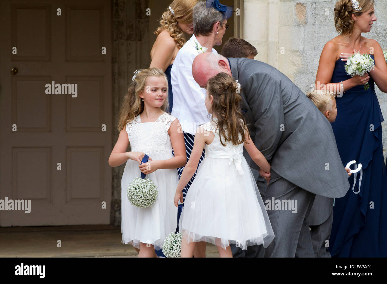 Two young bridesmaids face off whilst a grandfather intervenes Stock Photo