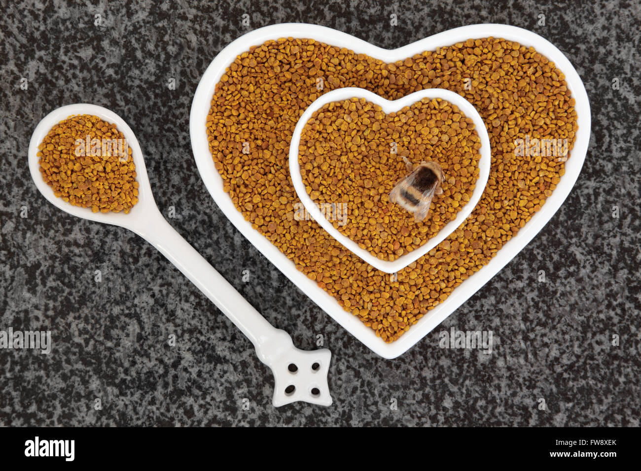 Bee pollen grain super food supplement in scoop and heart shaped dishes with bumblebee over marble background. Stock Photo