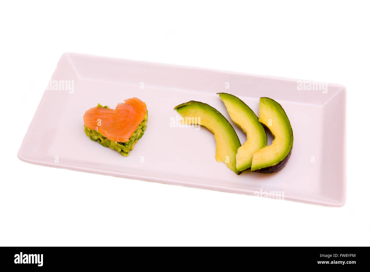 Tray with slices of avocado and salmon and avocado in a heart shape on white background Stock Photo