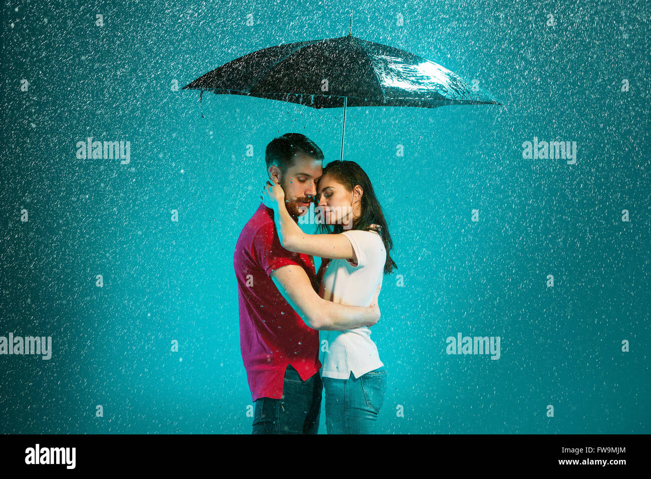 The loving couple in the rain with umbrella on a turquoise background ...