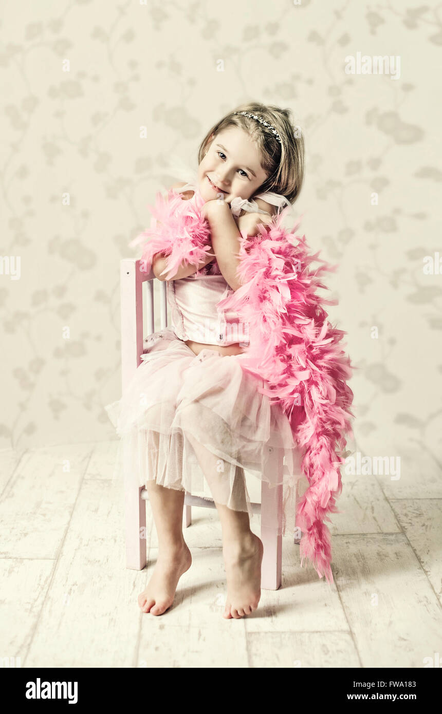 young girl in fancy dress sitting on wooden chair holding feather scarf and posing Stock Photo