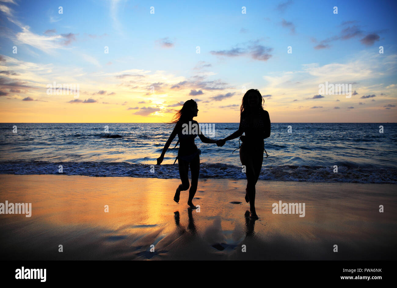 Two young happy women walking on tropical sea beach at sunset Stock ...