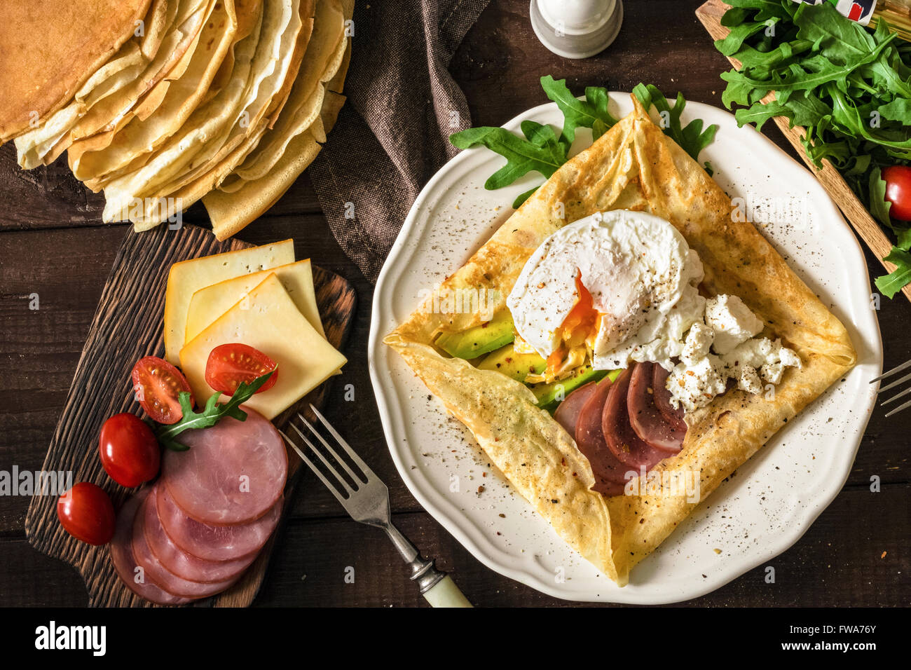 Crepe galette with meat, avocado, soft white cheese and poached egg on white plate Stock Photo