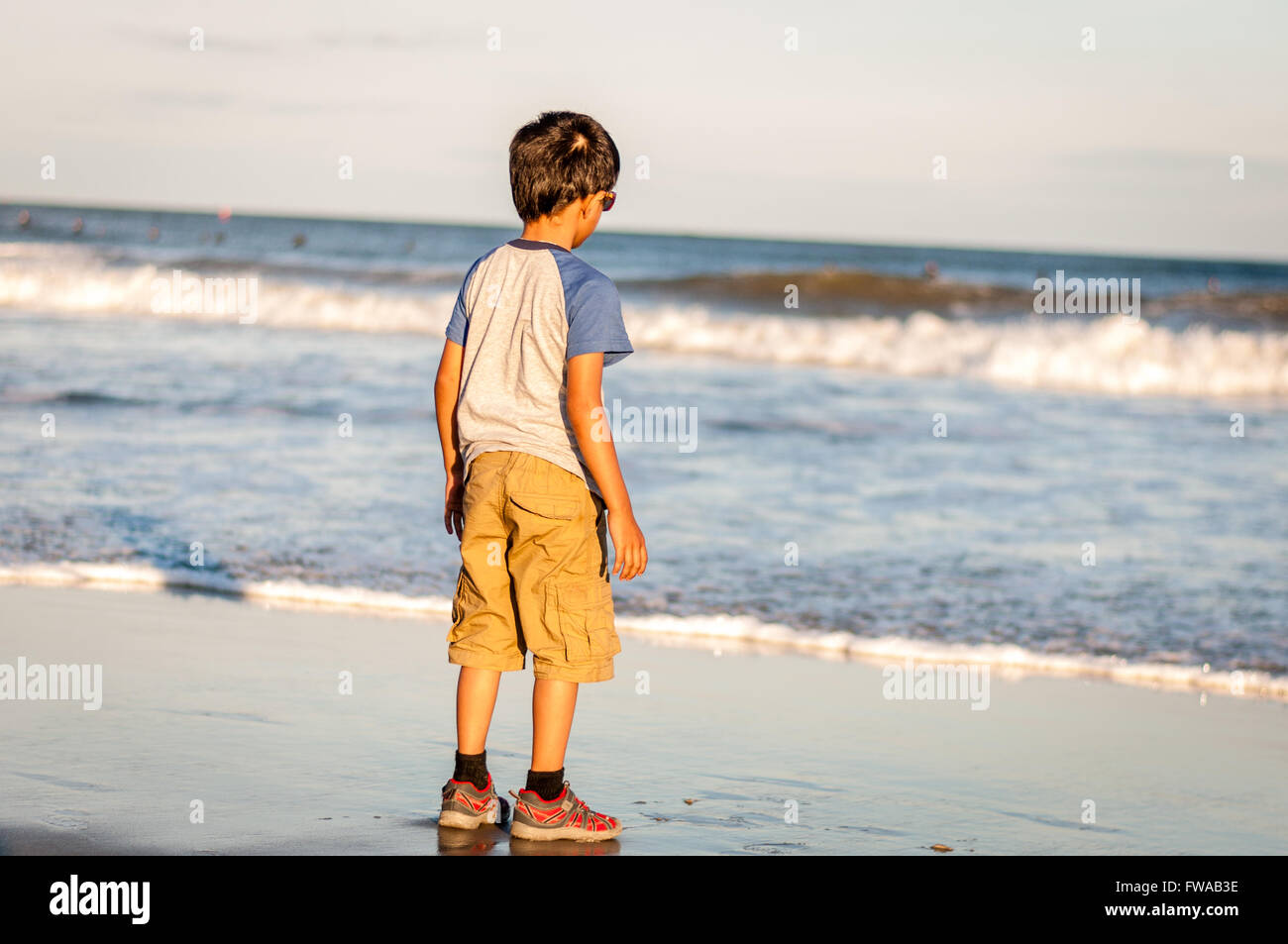 Little toddler boy standing on the Sand and looking at the sea water waves Stock Photo