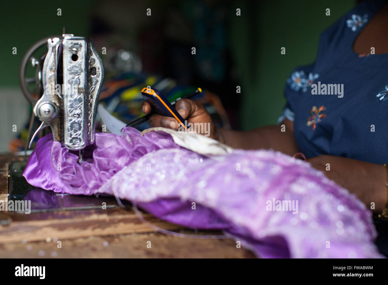 A female dress maker using a sewing machine and mobile phone, Nigeria, Africa Stock Photo