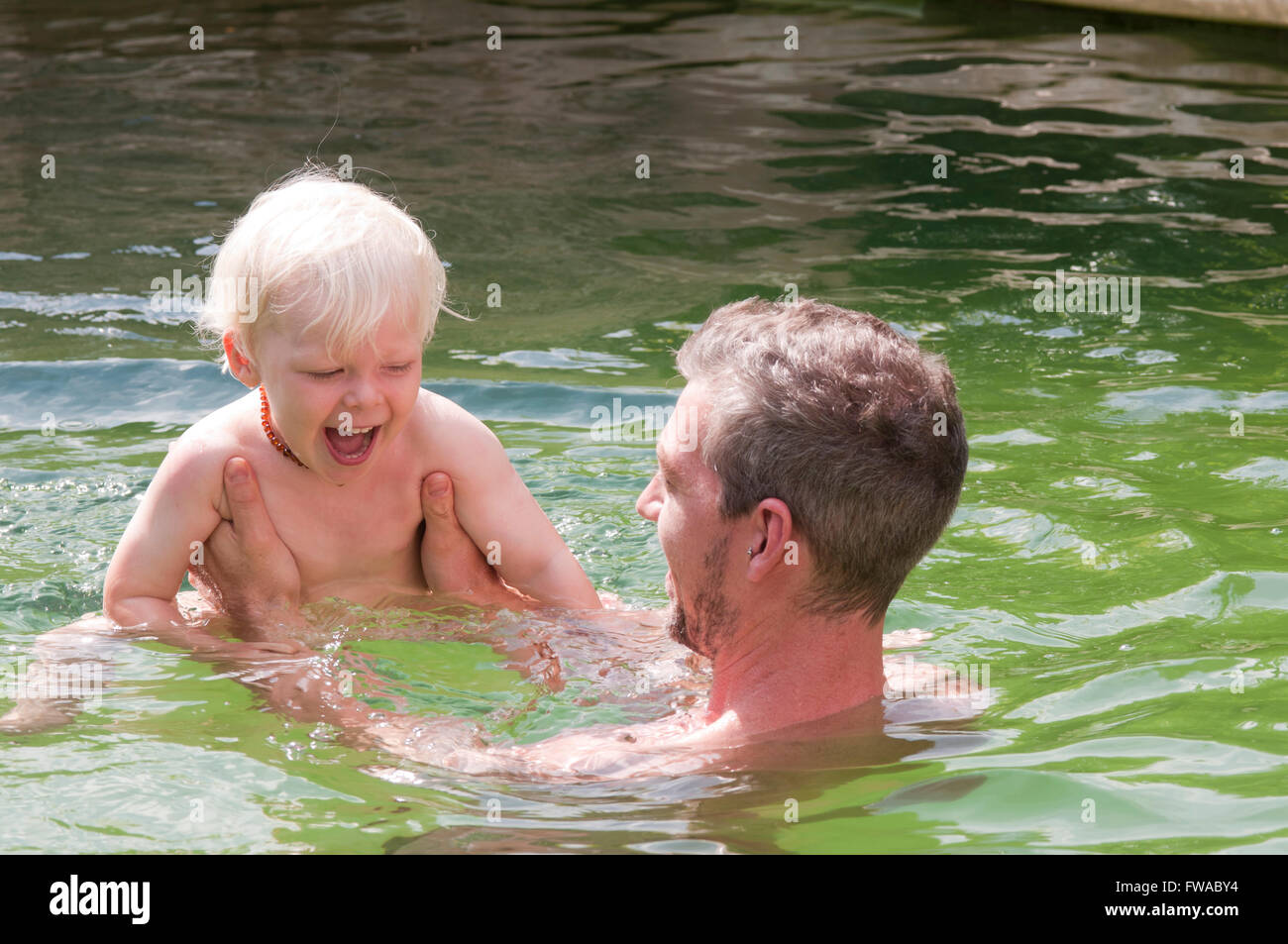 Father and son on holiday playing around in a swimming pool Stock Photo
