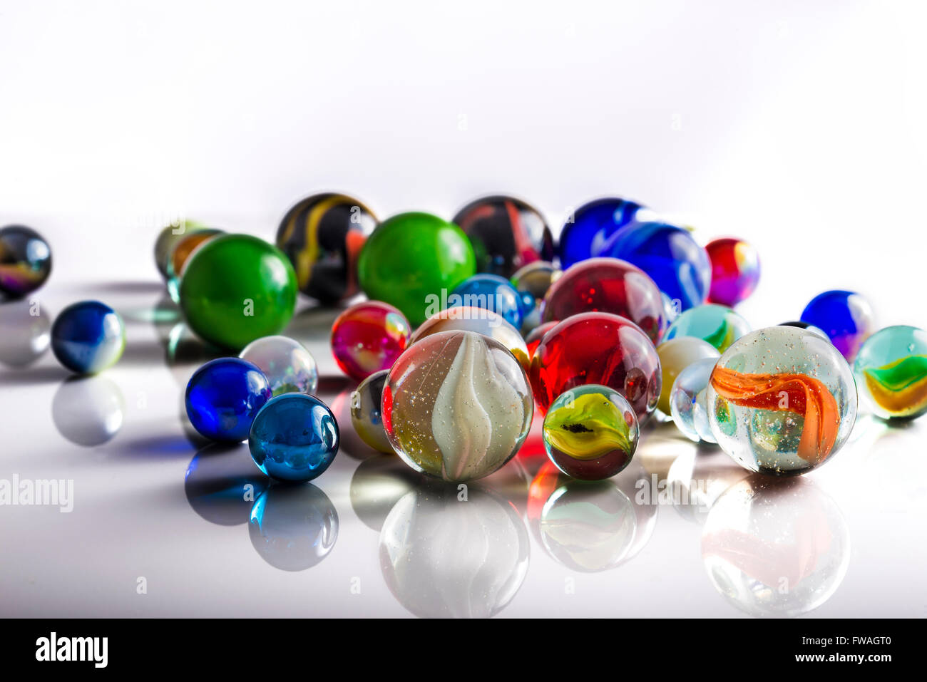 Group of mixed marbles on a reflective white surface Stock Photo