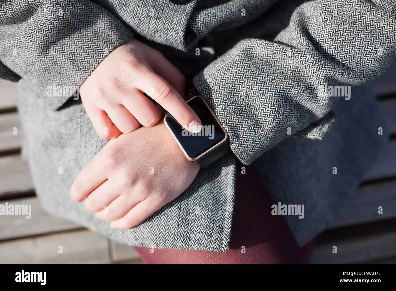 Hands of a female in grey coat browsing her modern smart watch. This person is always connected to social media and internet Stock Photo