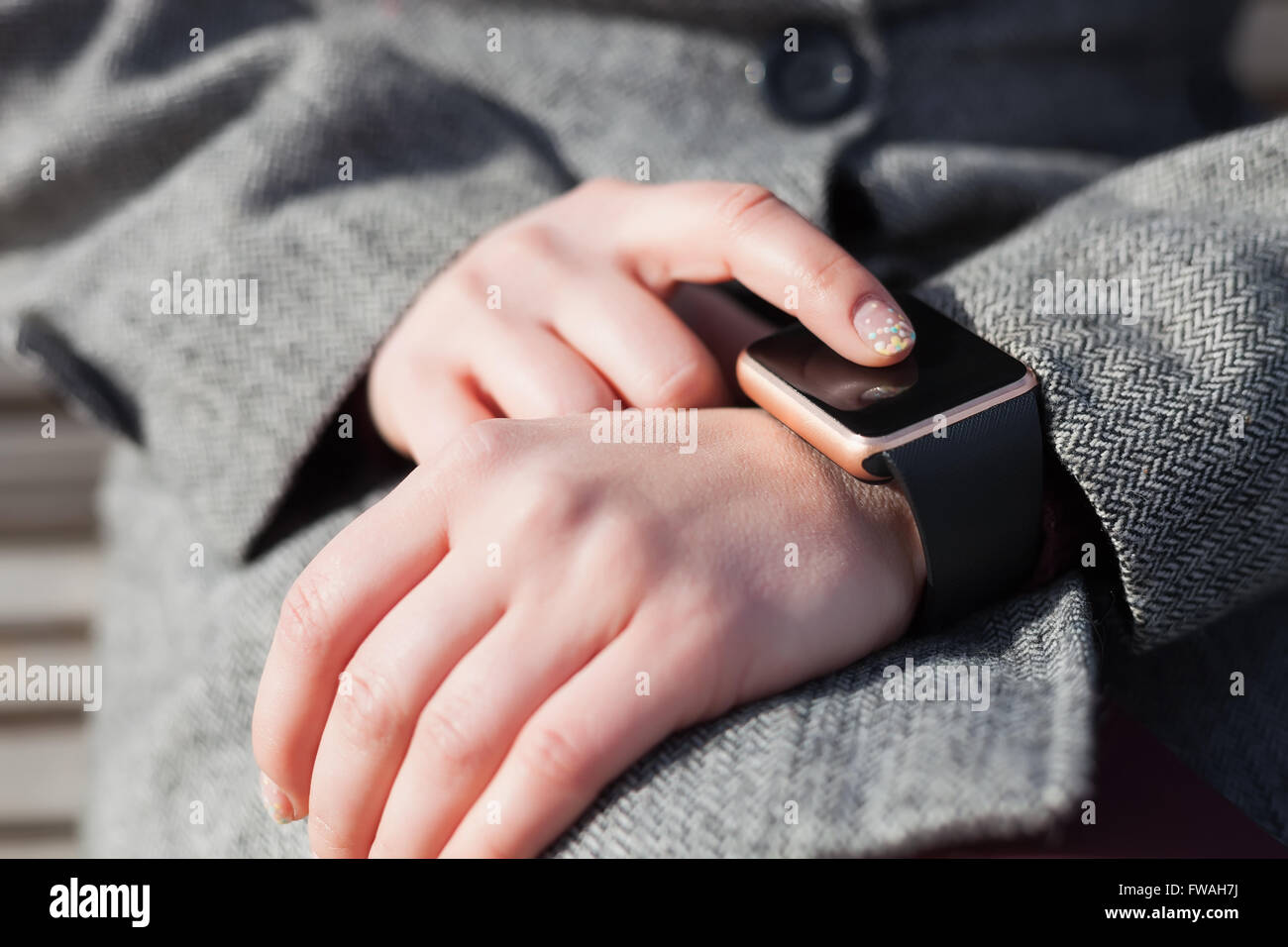 Hands of a female in grey coat browsing her modern smart watch. This person is always connected to social media and internet Stock Photo