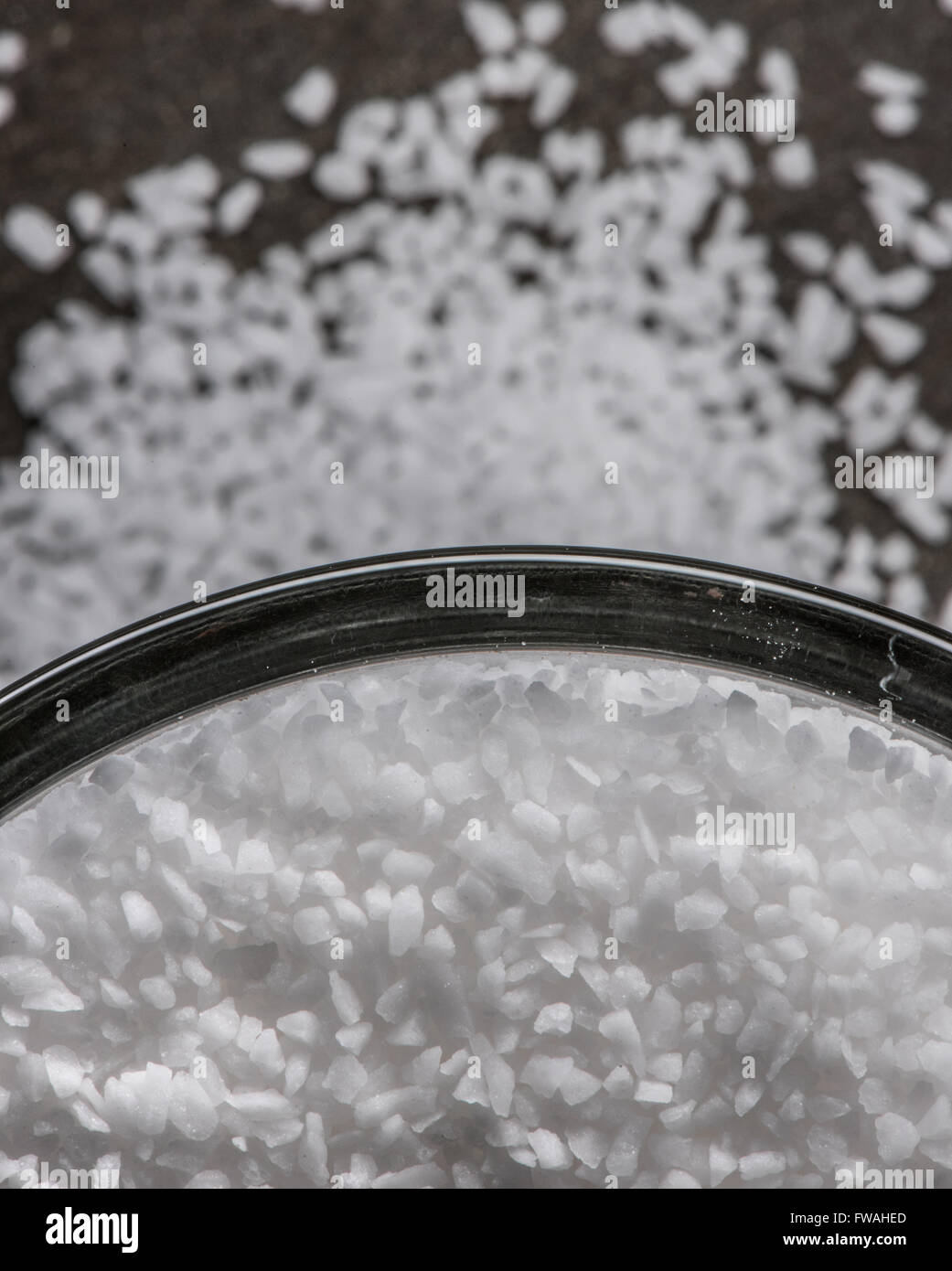 Sea salt in glass bowl with spill over onto slate cutting board background Stock Photo