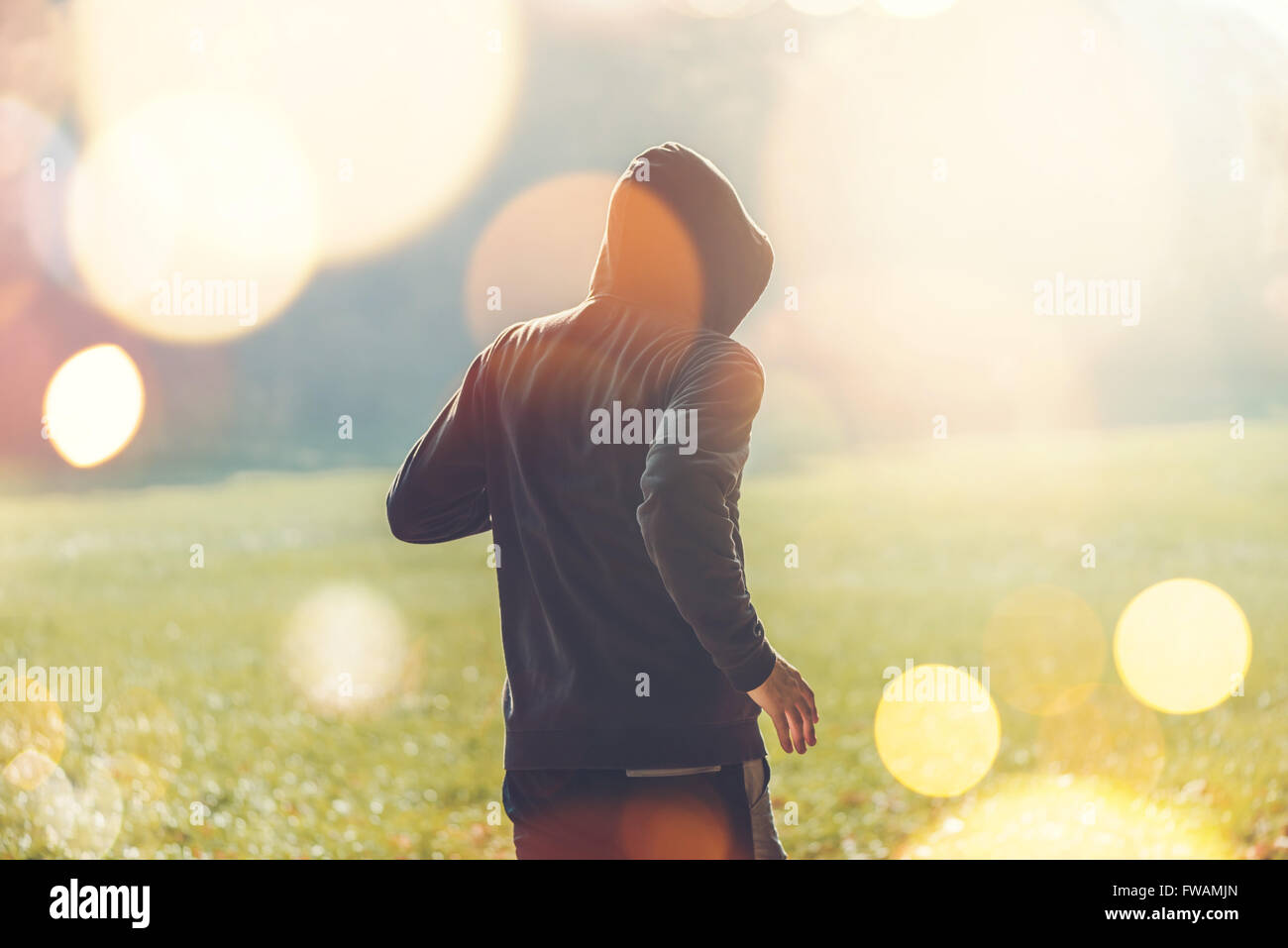 Unrecognizable hooded man jogging outdoors, healthy lifestyle activity in the park in early autumn morning, retro toned image Stock Photo