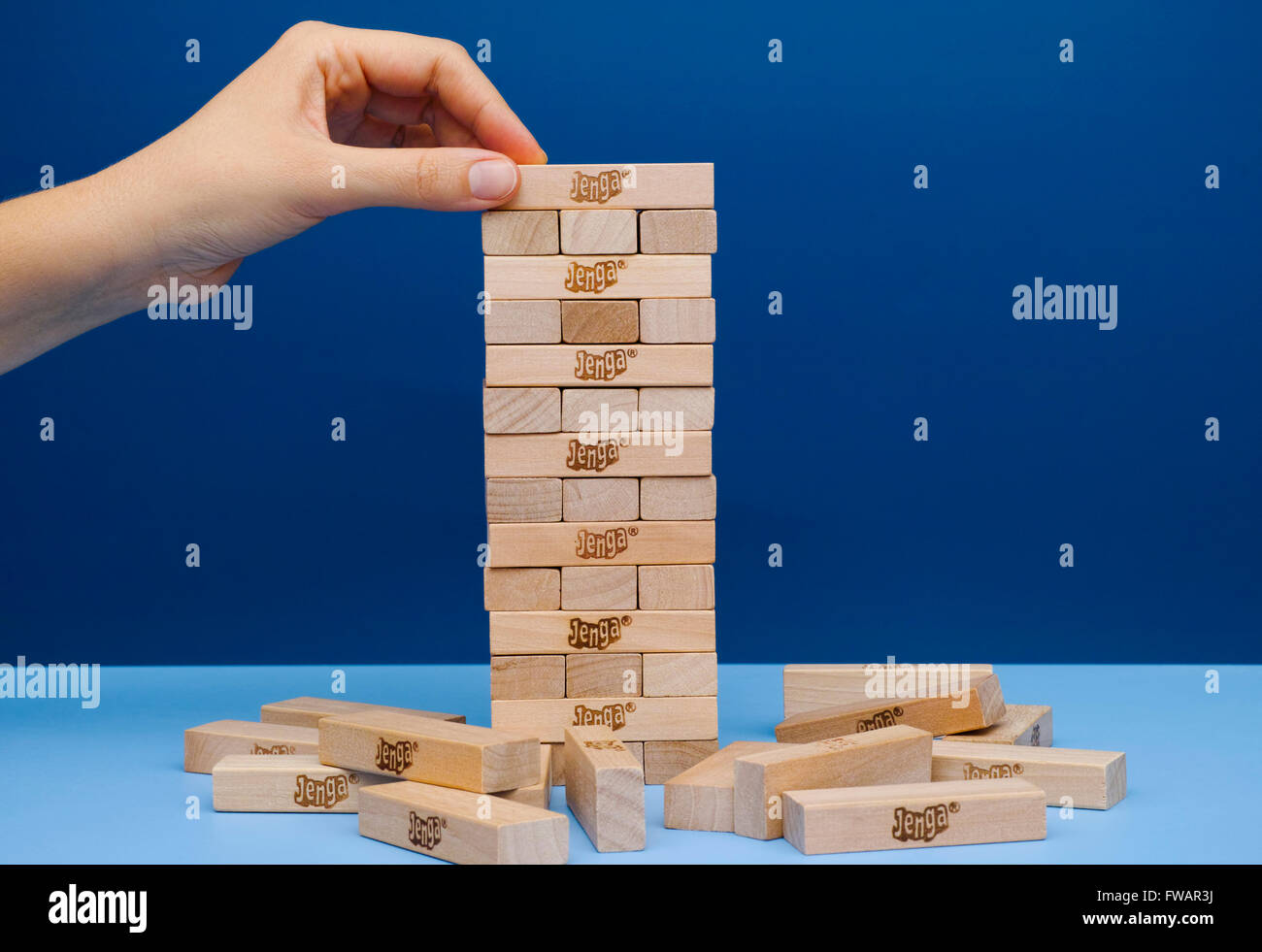 Tambov, Russian Federation - March 03, 2016 Player hand build Jenga tower constructed. Blue background. Studio shot. Stock Photo