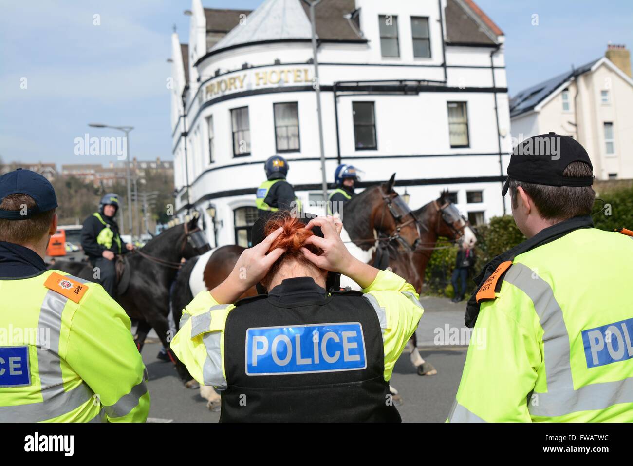 Dover, UK. 2nd April 2016. Clashes As Pro and Anti-refugee groups clash in Dover.  Police officer corrects her hair as mounted units march past. Credit: Marc Ward/Alamy Live News Stock Photo