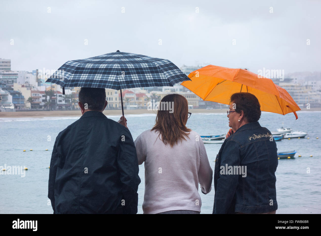 Las Palmas, Gran Canaria, Canary Islands, Spain, 3rd April 2016. Weather: With much of the UK forecast to have warm sunshine on Sunday and UK press saying 'hotter than Spain...', it`s a wet Sunday morning in Las Palmas on Gran Canaria as a band of rain sweeps over the city beach. PICTURED: People looking out over an empty Las Canteras beach in Las Palmas as rain comes down on a grey Sunday morning on Gran Canaria. Credit:  Alan Dawson News/Alamy Live News Stock Photo