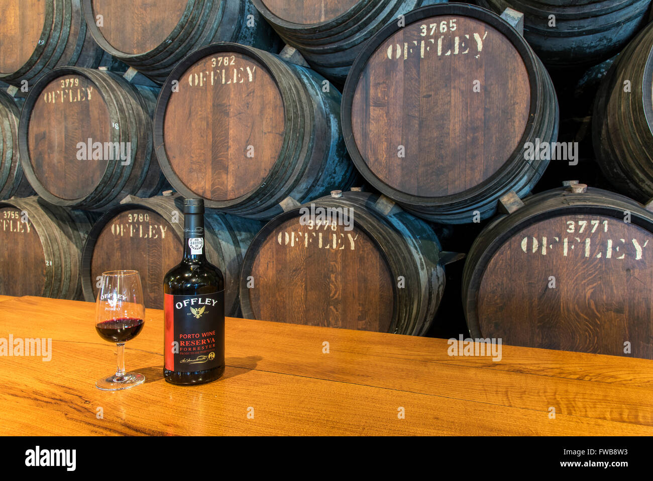 Bottle of Porto wine with glass and wine barrels behind at Offley wine cellars, Vila Nova de Gaia, Porto, Portugal Stock Photo