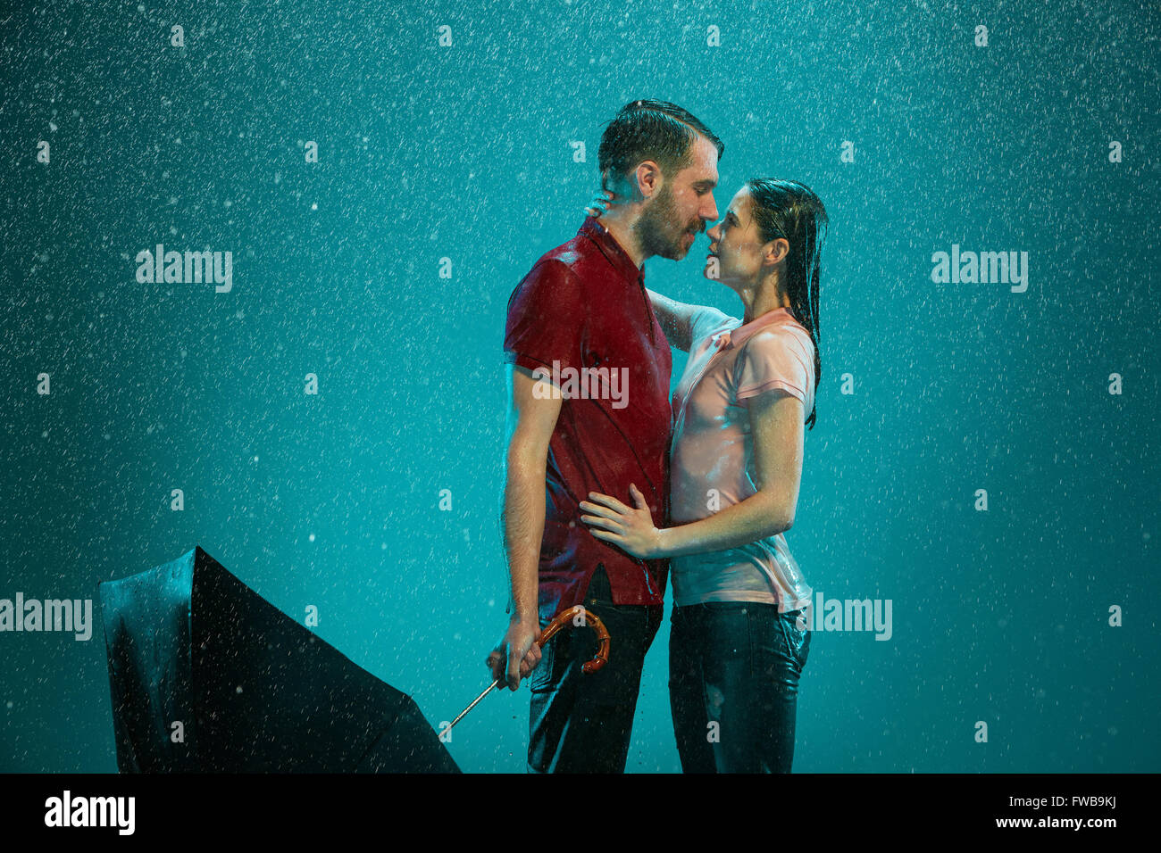 The loving couple in the rain with umbrella on a turquoise background ...
