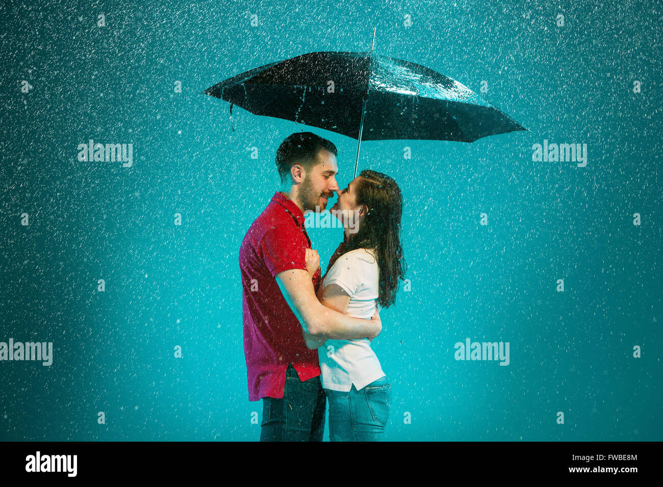 The loving couple in the rain with umbrella on a turquoise background ...