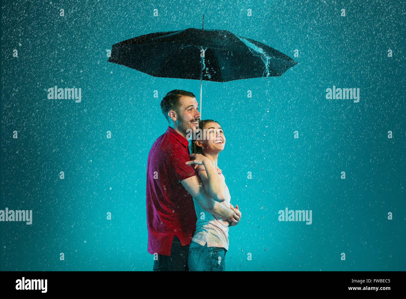 The loving couple in the rain with umbrella on a turquoise background ...