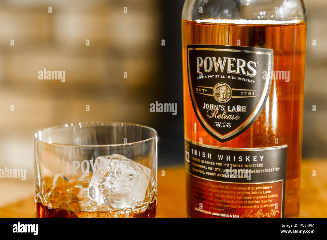 A bottle of Powers single pot still Irish whiskey with a glass of whiskey with ice cubes. Stock Photo