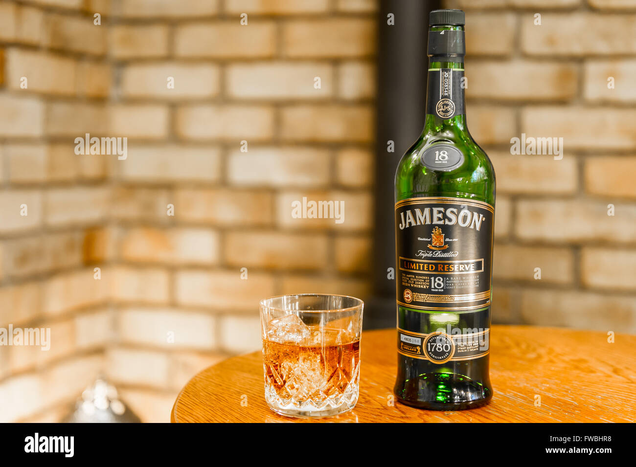 Bottle of 18 year old Jameson triple distilled limited reserve Irish whiskey with a glass of the whiskey with ice cubes on a table with copy space. Stock Photo