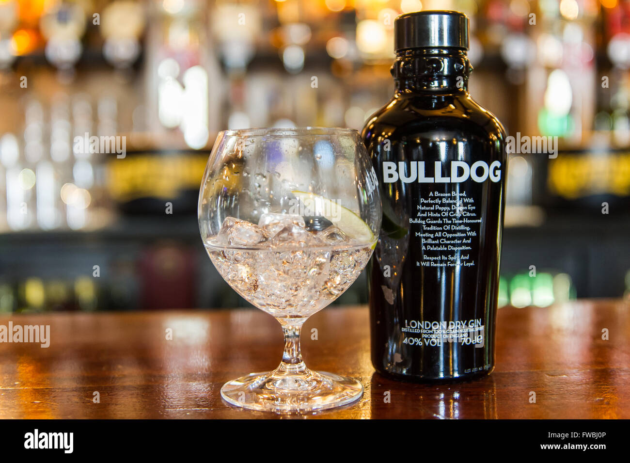 A bottle of Bulldog London Dry Gin and a glass of gin with ice cubes and lime on a bar counter top in Ireland. Stock Photo